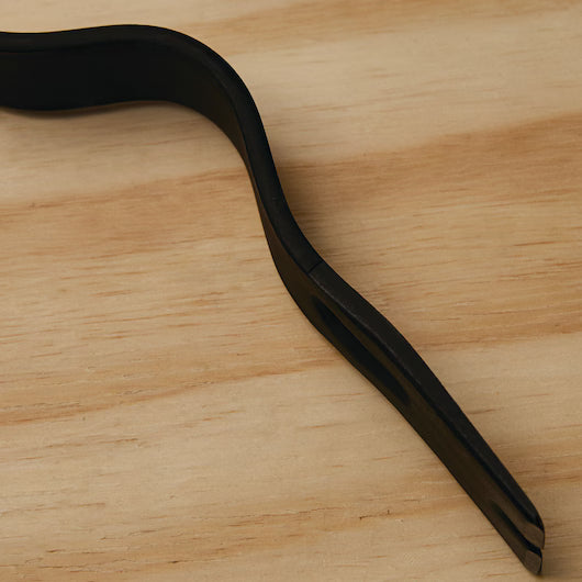 A close-up of the STANLEY® STEEL FLAT WONDER BAR® - 15IN by STANLEY, a black, wavy demolition tool, resting on a light wood surface.