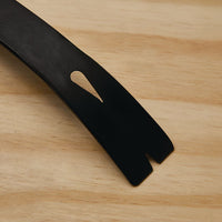 Close-up of the STANLEY 21 IN WONDER BAR® X21 PRY BAR on light wood, showing its black metal finish, angled notched end, and elongated teardrop-shaped hole near the tip for easy nail removal.
