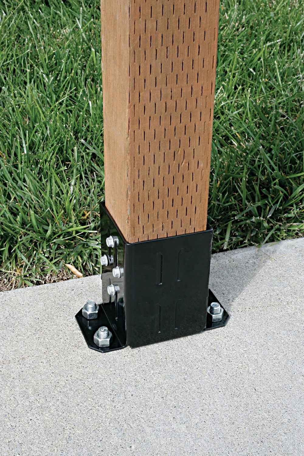 A Simpson Strong-Tie E-Z Base Black Powder-Coated Post Base secures a 4x4 wooden post to concrete with bolts, surrounded by green grass.
