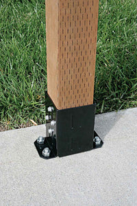 A Simpson Strong-Tie E-Z Base Black Powder-Coated Post Base secures a 4x4 wooden post to concrete with bolts, surrounded by green grass.