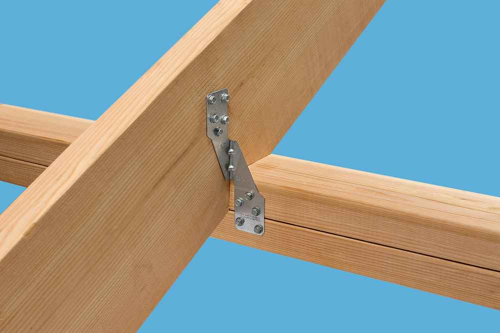 Close-up of a Simpson Strong-Tie H2.5A 18-Gauge ZMAX Galvanized Hurricane Tie connecting two wooden beams at a right angle with screws against a blue background, securely fastening the beams in place.
