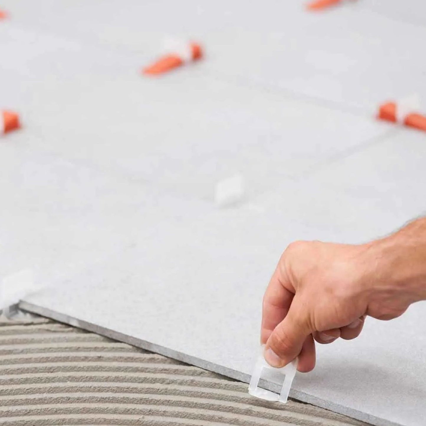 A skilled tiler uses the RAIMONDI 180BAS15B2200 RLS 1/16 in. HD Level Clips (2200-Pack) for setting large format tiles. These Raimondi clips ensure even spacing and alignment by being precisely placed between tiles on an adhesive-coated floor.