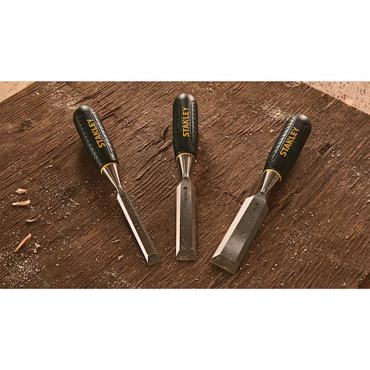 The STANLEY® WOOD CHISEL 3PC. SET (13,19,25MM) features three essential chisels on a workbench amid wood shavings—perfect tools for any craftsperson.