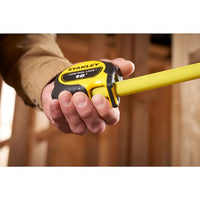 Someone uses a yellow STANLEY 16 ft. CONTROL-LOCK™ Tape Measure, extending the durable tool at a construction site with wooden framing in the background.