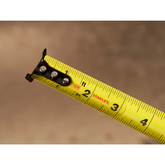 A close-up of the STANLEY 16 ft. CONTROL-LOCK™ Tape Measure, extended to show measurements from 1 to 4 inches, set against a blurred brown background.