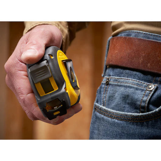 A person in jeans with a brown belt holds a STANLEY 25 ft. CONTROL-LOCK™ Tape Measure near their pocket.