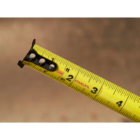 A close-up of the end of a STANLEY 30 ft. CONTROL-LOCK™ Tape Measure, extended to nearly 4 inches, shows clear black markings against a blurred brown background.