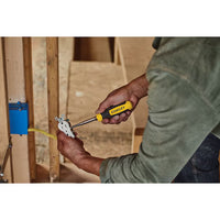 A person uses a STANLEY® QUICK CHANGE INTERCHANGEABLE SCREWDRIVER 6-IN-1 to install or adjust an electrical outlet in a wall frame with exposed wooden studs and wires.
