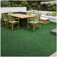 Modern outdoor patio with a pet-friendly TrafficMaster Emerald Green Precut Turf 6 ft. x 8 ft. Artificial Grass Rug, wooden dining table, green cushioned chairs, white sectional sofa with colorful pillows, and lush landscaping with green plants and shrubs.