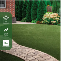 A landscaped yard features the TrafficMaster Emerald Green Precut Turf 6 ft. x 8 ft. Artificial Grass Rug, with a curved stone path and bushes by a brick house. Icons show UV resistance, light traffic suitability, and 8 oz face weight.