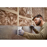 A man wearing safety glasses and gloves uses a STANLEY® Light-duty Steel Staple Gun to fasten reflective insulation to a wall with exposed fiberglass insulation and wooden framing.