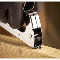 A gloved hand uses the STANLEY® Light-duty Steel Staple Gun to secure a staple into a piece of light-colored wood.