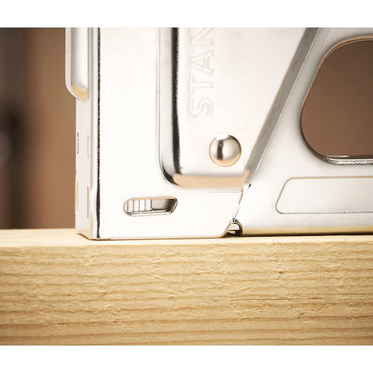 Close-up of a STANLEY® Light-duty Steel Staple Gun by STANLEY pressed against a light wooden plank, ready for use.