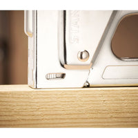 Close-up of a STANLEY® Light-duty Steel Staple Gun by STANLEY pressed against a light wooden plank, ready for use.