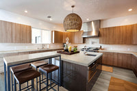 Modern kitchen featuring wooden cabinets, a large island with three stools, stainless steel appliances, a woven pendant light, decorative jars on the island, and Msisurfaces Akadia Luxury Vinyl Plank scratch-resistant flooring.