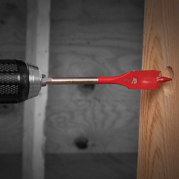 The Diablo DIABLO DSP2930-S9 9-Piece Spade Bit Set, featuring a red SPEED-TIP design, efficiently drills into wood against an unfinished wall backdrop, ideal for construction or woodworking. This Impact Strong tool guarantees precision and durability for challenging projects.