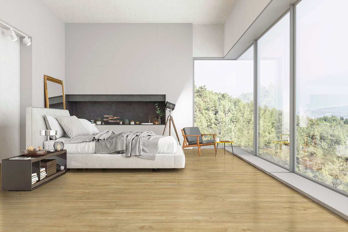 Modern bedroom with large bed, nightstand, and armchair boasts floor-to-ceiling windows overlooking forest. MSI Cyrus Brookline Luxury Vinyl Planks (23.77 sqft/box) offer 100% waterproof, click-lock installation for a minimalist look.