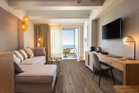 A modern hotel room with a sofa, desk, wall-mounted TV, and pendant lights. Sliding glass doors lead to a sea-view balcony. Warm neutral tones and MSI Cyrus Fauna Luxury Vinyl Planks create a cozy feel with durable CrystaLux™ protection.