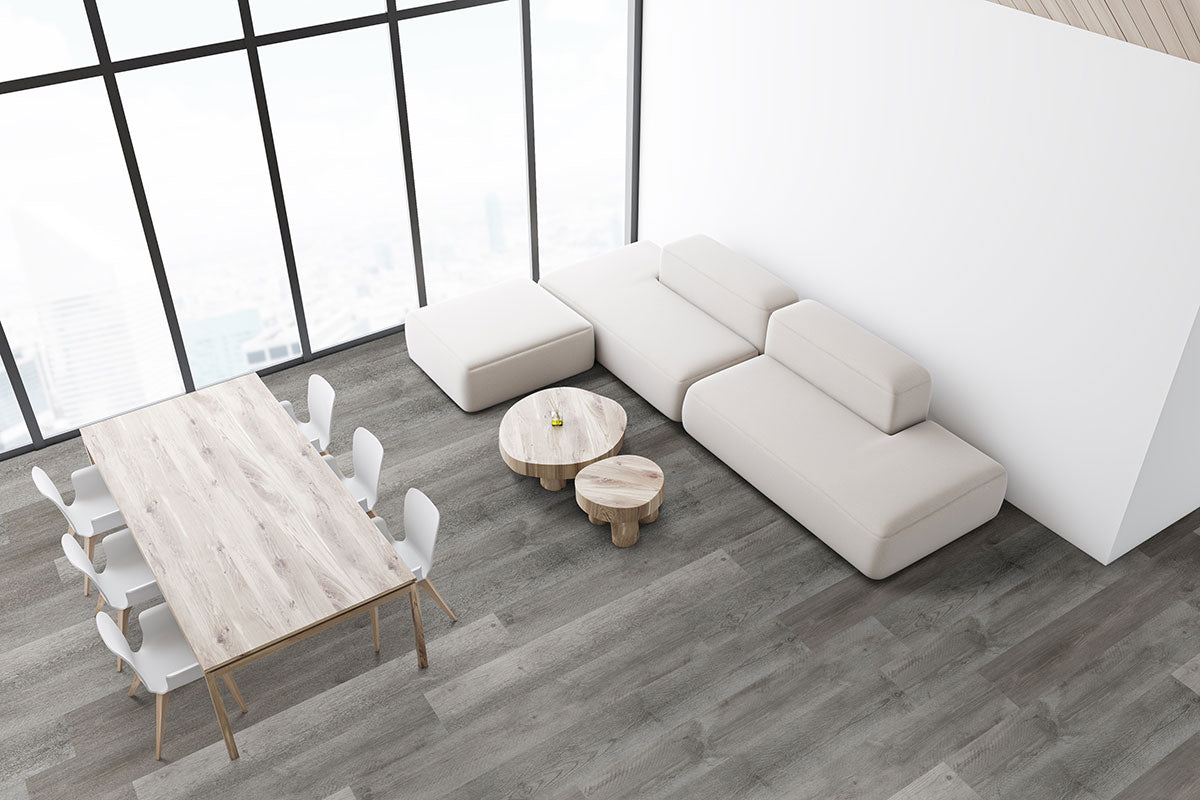 Modern, minimalist living space featuring a light beige sectional sofa, wooden coffee tables, dining set with six white chairs, floor-to-ceiling windows, and MSI Katella Luxury Vinyl Planks flooring in elegant gray wood tones.