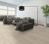 Modern living room with MSI Cyrus Runmill Isle Luxury Vinyl Planks (23.77 sq ft/box), featuring CrystaLux protection, a dark gray sectional, black floor lamp, coffee table, potted plant, and a large window framing a city view with natural light.