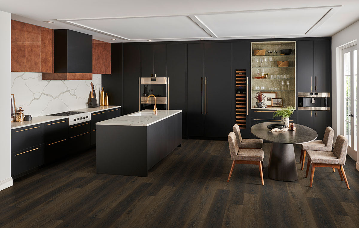 Modern kitchen with matte black cabinets, marble island, built-in appliances, and a round dining table. MSI Cyrus Barrell Luxury Vinyl Planks (CrystaLux™ wear layer) add durability, complemented by warm wood and marble accents.