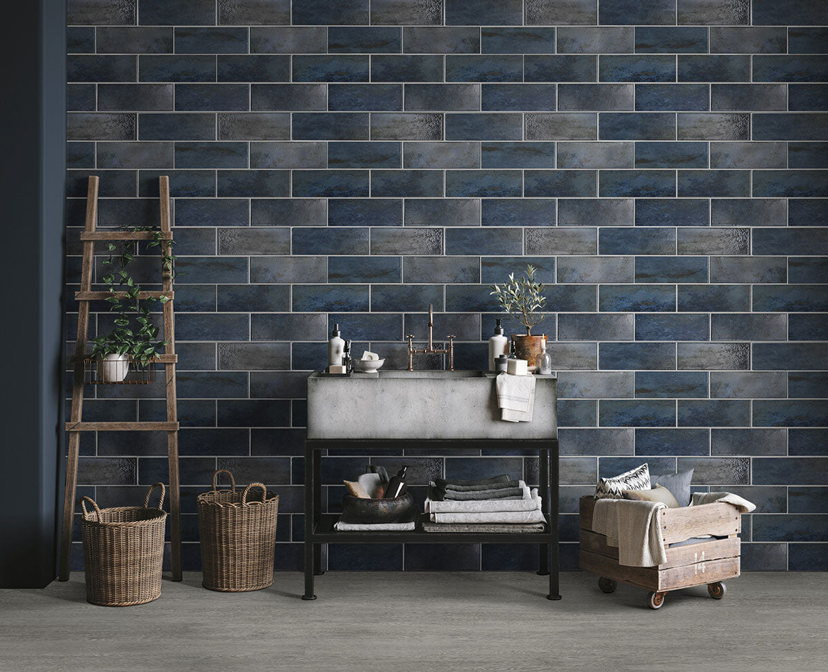 A modern room featuring Cyrus Grayton Luxury Vinyl Planks by MSI, with a blue brick tile wall, concrete sink on a black metal stand, shelves with towels and bottles, a wooden ladder, wicker baskets, and a wooden cart.