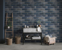 A modern room featuring Cyrus Grayton Luxury Vinyl Planks by MSI, with a blue brick tile wall, concrete sink on a black metal stand, shelves with towels and bottles, a wooden ladder, wicker baskets, and a wooden cart.