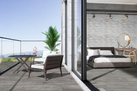 A modern bedroom with MSI Katella Luxury Vinyl Planks flooring opens to a balcony with glass railing, two chairs, and a round table. Inside are a gray bed, wooden furniture, a decorative wall, and a large potted plant outside.