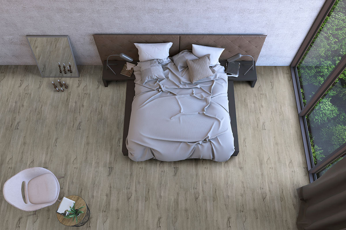 Top-down view of a modern bedroom with an unmade bed, bedside tables with lamps, MSI Cyrus Dunite Oak Luxury Vinyl Planks flooring, large window with greenery, a chair and small round table, and a floor mirror against the wall.