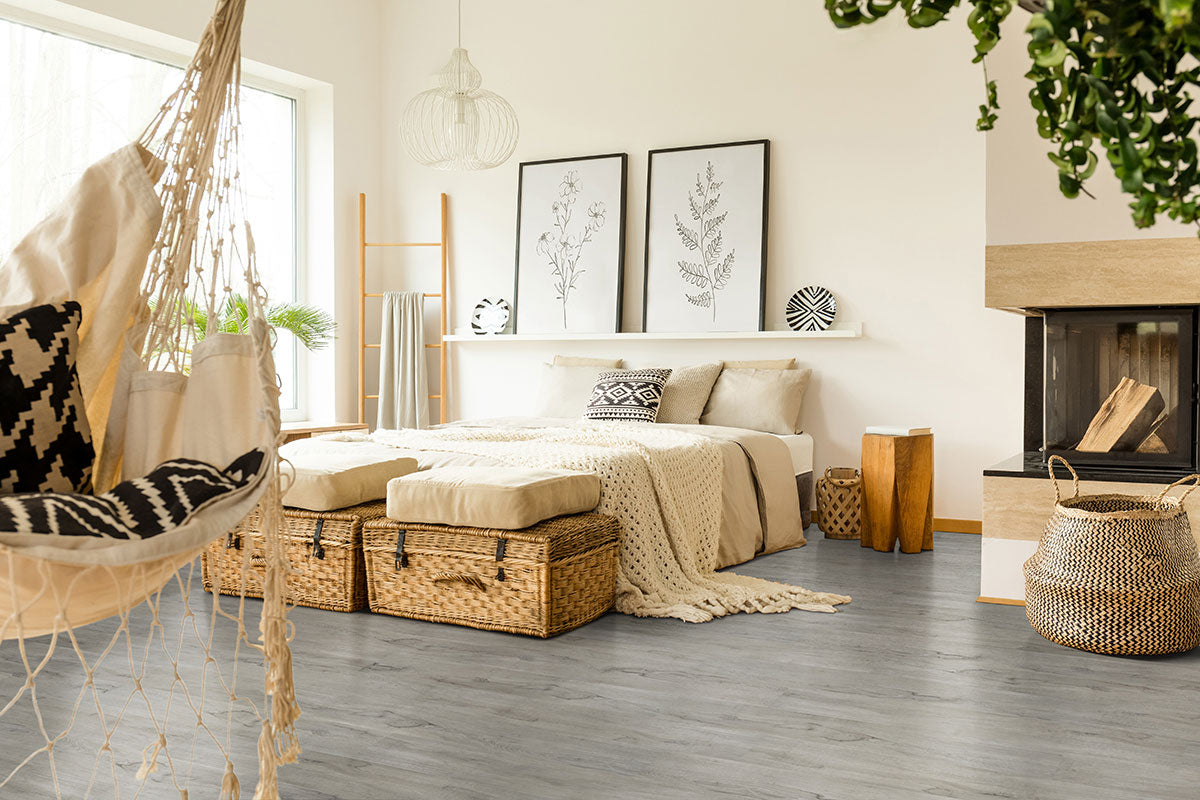 Bright, cozy bedroom with neutral tones, a hammock chair, wicker baskets, knit blankets and patterned pillows, plants, botanical prints, modern fireplace, and easy-to-install waterproof MSI Cyrus Dunite Oak Luxury Vinyl Planks flooring.
