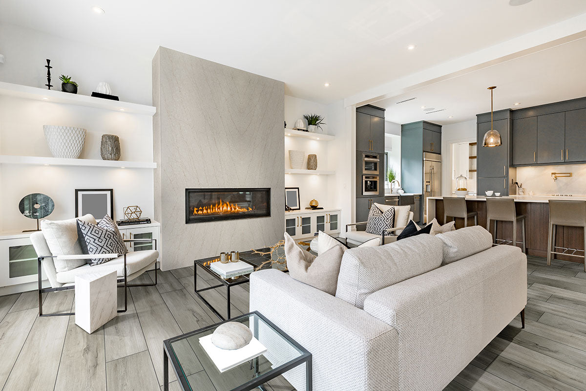 A modern living room features MSI XL Cyrus Dunite Oak Luxury Vinyl Planks, showcasing stylish flooring with a CrystaLux™ wear layer and waterproof SPC core, flowing into an open kitchen with dark cabinets and pendant lighting.