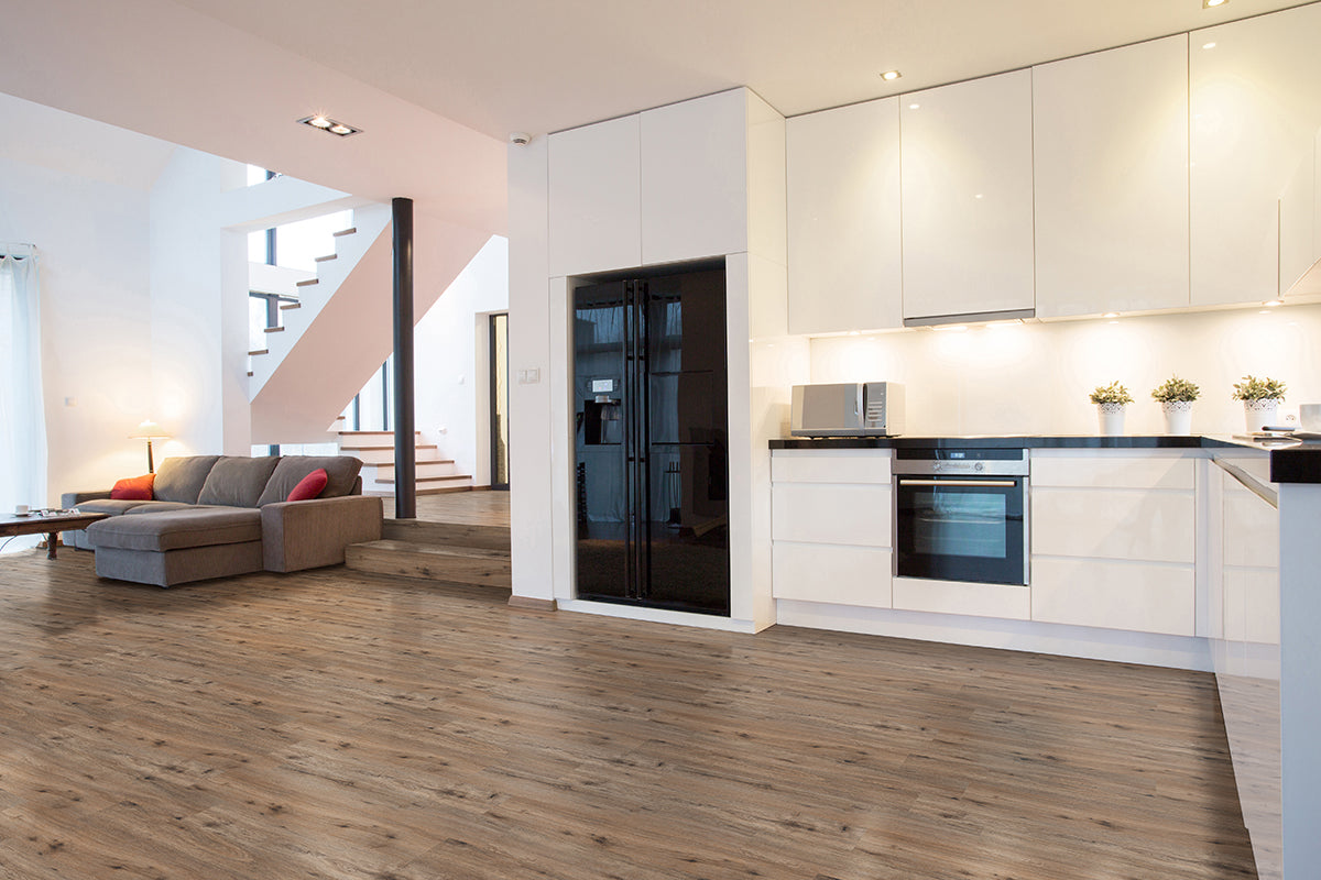 Modern open-plan kitchen and living area with white cabinets, black appliances, a gray sofa, coffee table, stairs to an upper floor, and MSI Cyrus Fauna Luxury Vinyl Planks (BOX – 23.77 SQFT) for durable flooring with CrystaLux™ protection.
