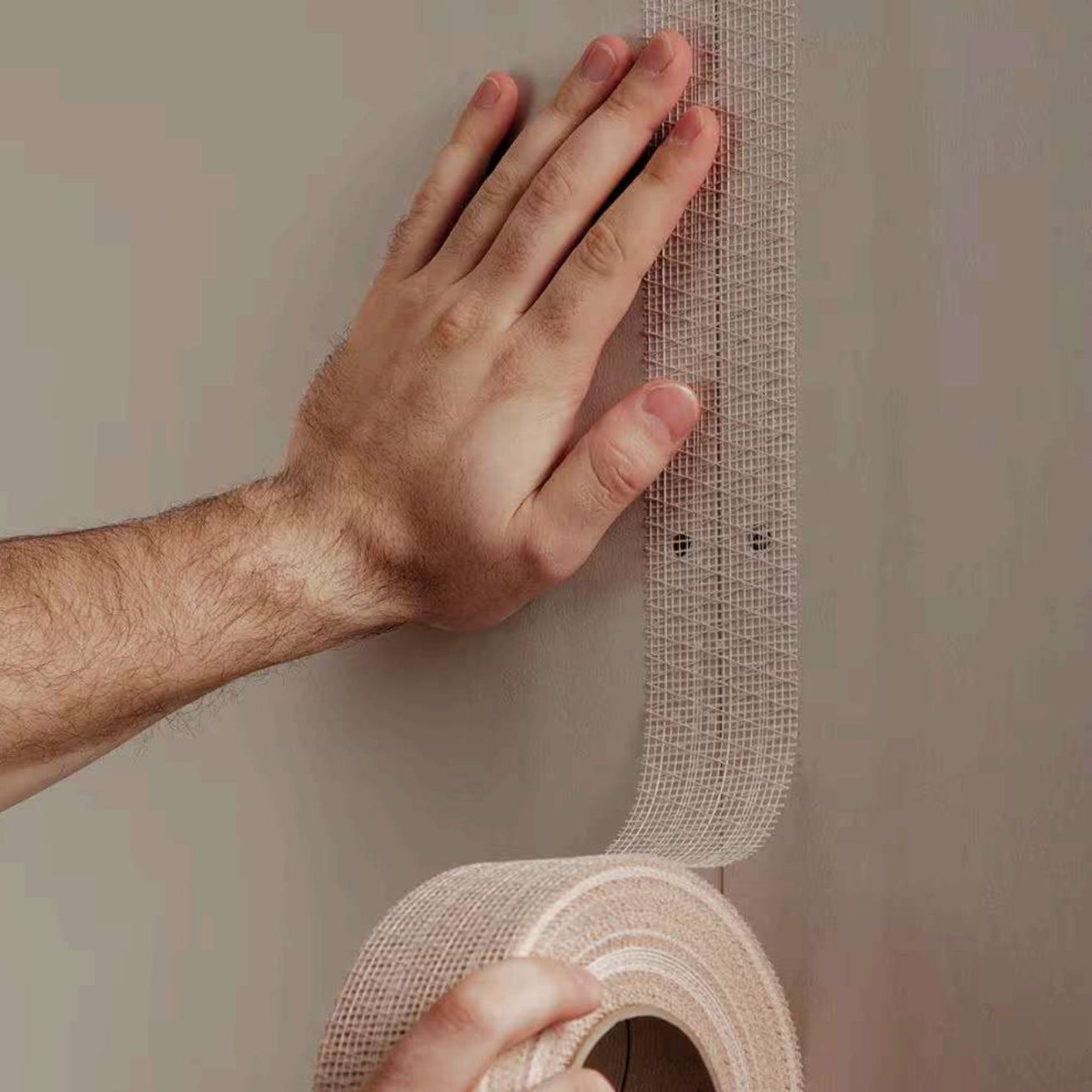 A person applies ADFORS FibaTape FDW8666-U 2-3/8 in. x 250 ft. Extra Strength Reinforced Drywall Tape vertically, smoothing it with one hand and holding the roll with the other for strong drywall seam reinforcement.