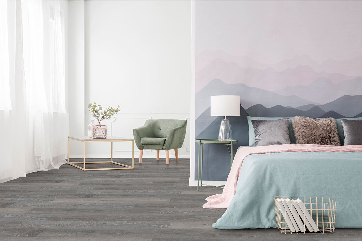 A modern bedroom with a pastel mountain mural, blue and pink bedding, a white lamp on a green nightstand, green armchair, MSI Cyrus Finely Luxury Vinyl Planks flooring with CrystaLux™ wear layer, and large windows with sheer curtains.