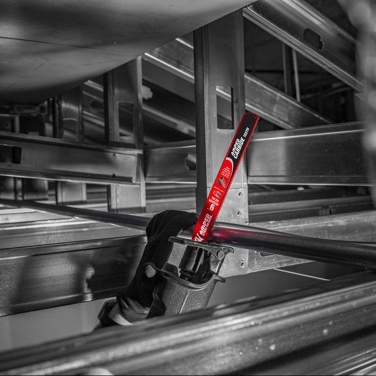 In a grayscale industrial setting, an individual skillfully uses a Diablo reciprocating saw fitted with a DIABLO DS0610CFA3 AMPED Steel Demon 6 in. 10TPI blade, cutting through a metal rod effortlessly among stacked steel beams, showcasing the tools precision and efficiency.