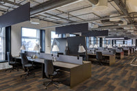 A modern open-plan office with rows of desks, chairs, and lamps features MSI Cyrus Hawthorne Luxury Vinyl Planks (23.77 SQFT/box) with a CrystaLux™ wear layer. Large windows and exposed ceilings create an industrial yet organized atmosphere.
