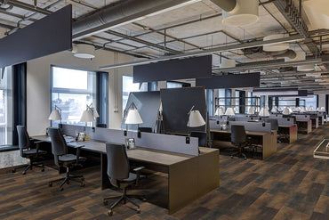 A modern open-plan office with rows of desks, chairs, and lamps features MSI Cyrus Hawthorne Luxury Vinyl Planks (23.77 SQFT/box) with a CrystaLux™ wear layer. Large windows and exposed ceilings create an industrial yet organized atmosphere.