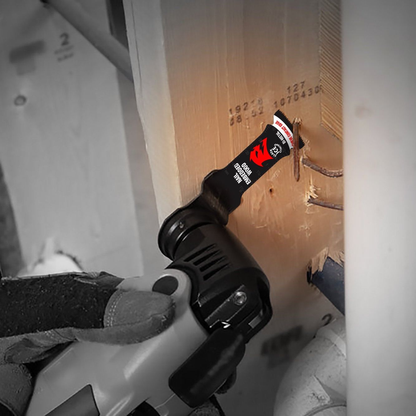 While wearing protective gloves, a person skillfully uses a Diablo Demo Demon™ oscillating blade with an ultra-hardened edge and black handle to slice through wood. The red and black label adds distinction as the tool moves precisely amid pipes and construction materials in the background.