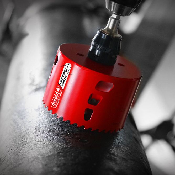 The DIABLO DHS1250CT 1-1/4 in. Carbide Teeth Hole Saw for Wood and Metal by Diablo is attached to a drill on a metal pipe, with its increased productivity and longer cutting life emphasized against a blurred background.