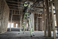 A construction worker in safety gear stands on a LITTLE GIANT 17117 CONQUEST 2.0 1A 7.5-15 F/G ARTICULATED EXTENSION LADDER, working on exposed wiring inside a building with unfinished wooden framing.