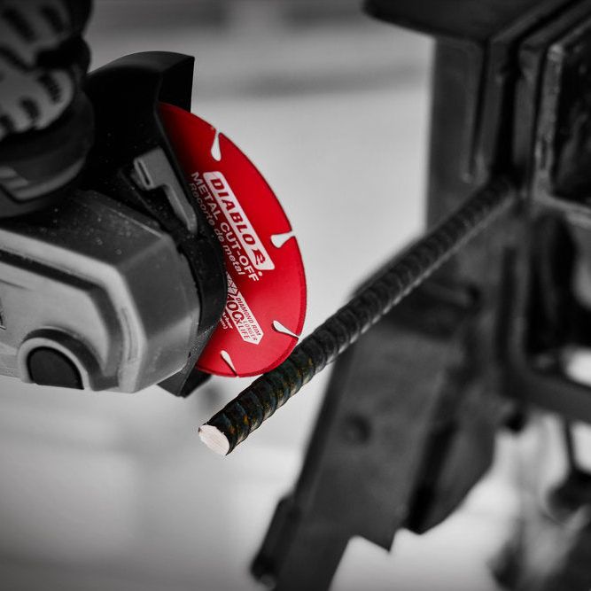 A close-up shows the DIABLO DDD070DIA101F 7 in. Diamond Metal Cut-Off Disc from Diablo, with a red cutting disc slicing through metal rebar effortlessly. The black-and-white backdrop highlights durability and the diamond disc design hints at superior cutting life, with the Diablo brand visible.