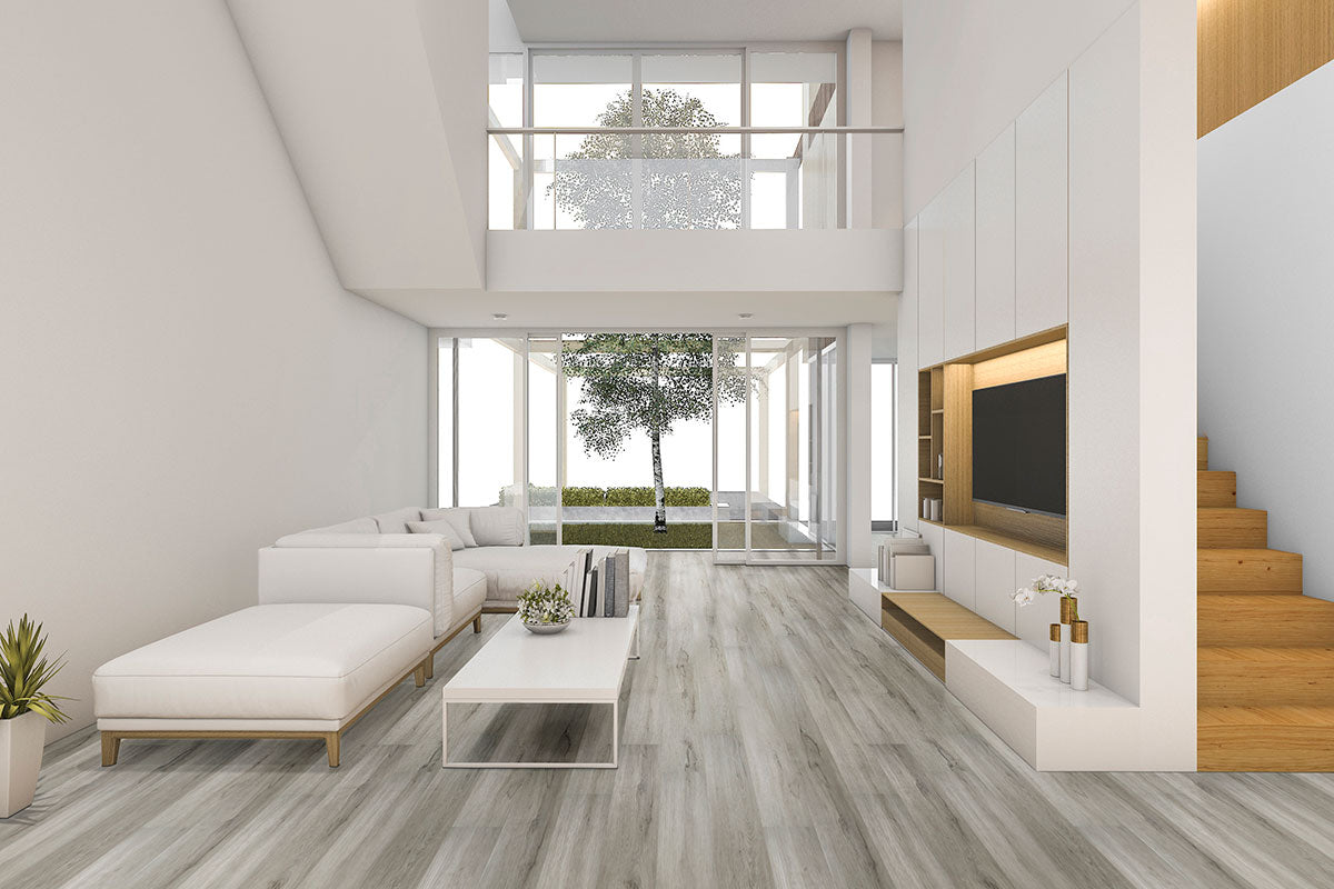 A bright, modern living room features MSI Cyrus Dunite Oak Luxury Vinyl Planks (23.77 sq ft per box), waterproof flooring in light wood tones. White furniture, built-in shelves, large garden-view windows, and a wooden stairway complete the space.