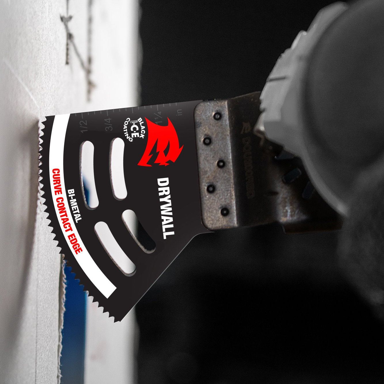 A close-up of the Diablo DOS200RBD 2 in. Starlock Bi-Metal Oscillating Blade for Drywall with Black I.C.E coating in action; the blade, adorned with white and red branding, shows Drywall and Guide Threaded Edge. A gloved hand grips the handle firmly.