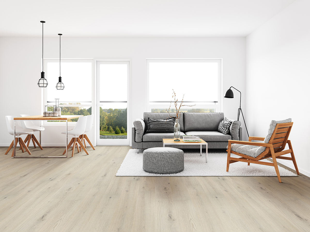 Bright, modern living and dining area with MSI Cyrus Runmill Isle Luxury Vinyl Planks featuring CrystaLux protection, white walls, gray sofa, armchair, pouf, floor lamp, coffee table, dining table with white chairs, large windows, and pendant lights.