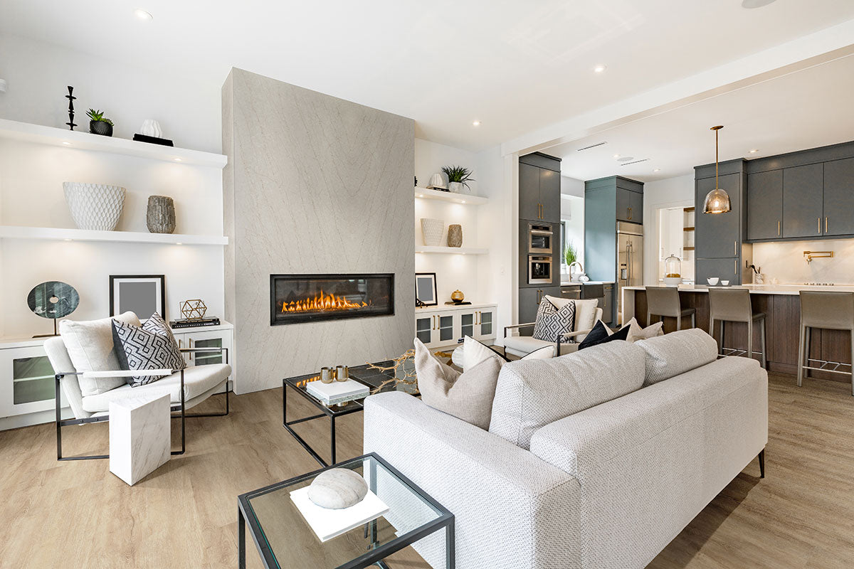 Modern living room with a light gray sofa, glass coffee tables, and built-in fireplace. Open shelves with décor and MSI Cyrus Sandino Luxury Vinyl Planks flooring flow into the kitchen with sleek gray cabinets for a chic look.