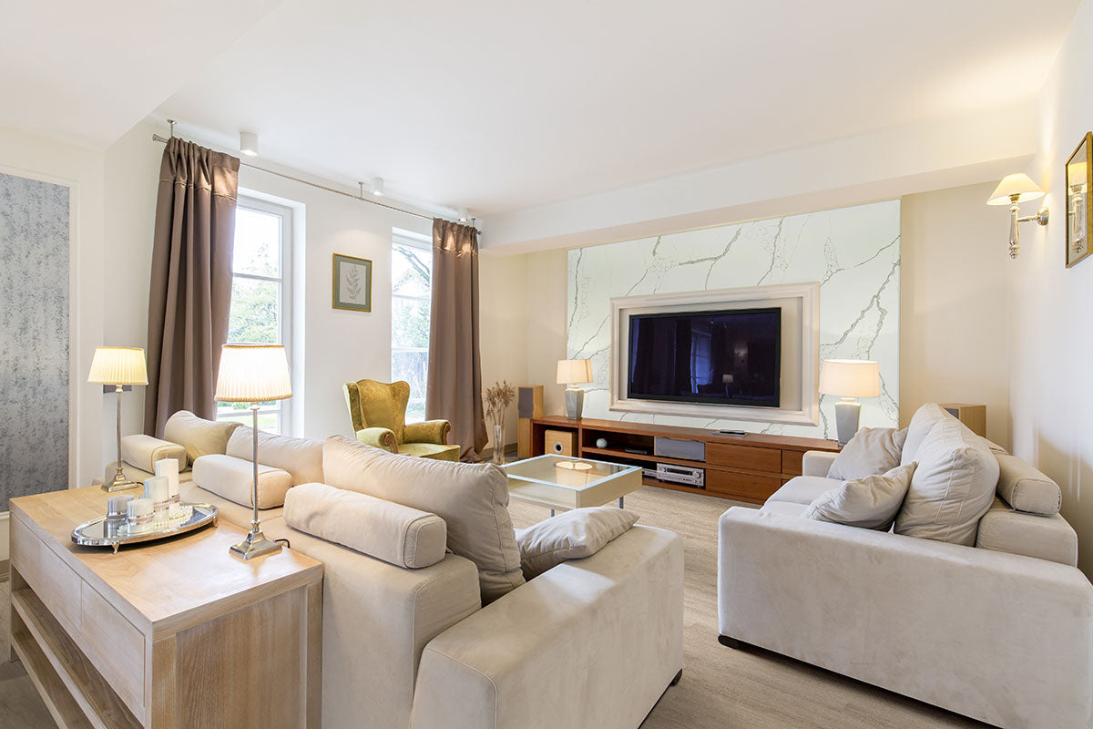 A spacious, modern living room with beige sofas, a glass coffee table, a green armchair, floor lamps, MSI Cyrus Sandino Luxury Vinyl Planks flooring (waterproof SPC core), a wall-mounted TV, and windows with curtains letting in natural light.