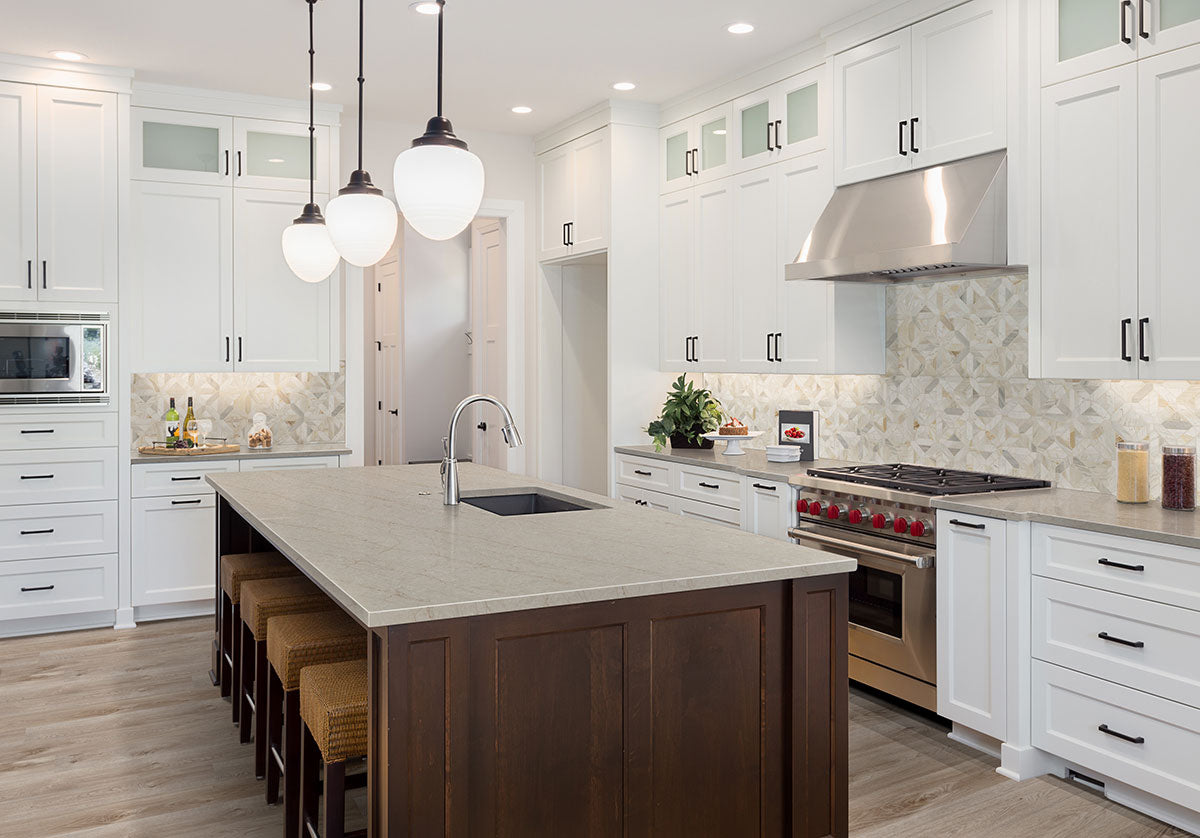A modern kitchen with white cabinets and stainless steel appliances features MSI Cyrus Whitfield Gray Luxury Vinyl Planks, woven stools, pendant lights, a dark wood island, and a patterned tile backsplash for a bright, clean look.