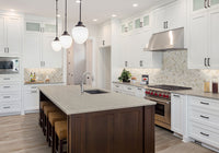 A modern kitchen with white cabinets and stainless steel appliances features MSI Cyrus Whitfield Gray Luxury Vinyl Planks, woven stools, pendant lights, a dark wood island, and a patterned tile backsplash for a bright, clean look.