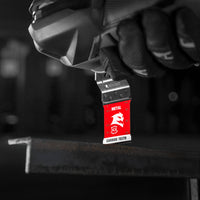 A gloved hand holds a Diablo DIABLO DOS125CF3 Starlock power saw with a red blade labeled Metal and Carbide Teeth, poised above a metal beam, against a dark, blurred background, highlighting its precision in cutting.