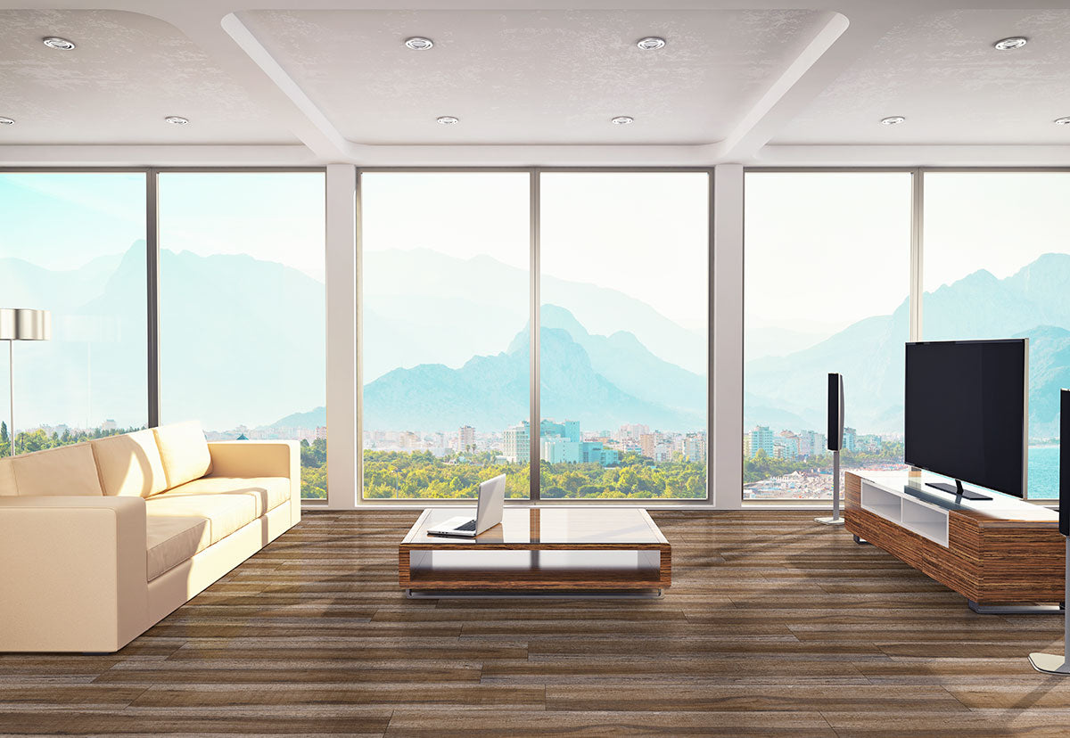 Modern living room with CrystaLux™ floor-to-ceiling windows, beige sofa, coffee table, flat-screen TV, and MSI XL Cyrus Exotika Luxury Vinyl Planks (22.44 sqft). Enjoy scenic mountain and city views under a clear sky through waterproof CrystaLux™ glass.